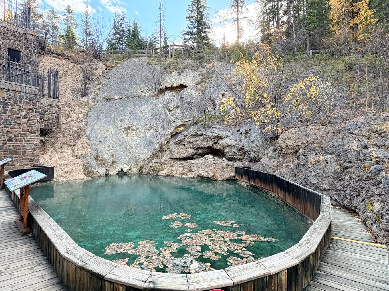 The Cave and Basin thermal pool in autumn with mineral deposits on the surface below a rock face